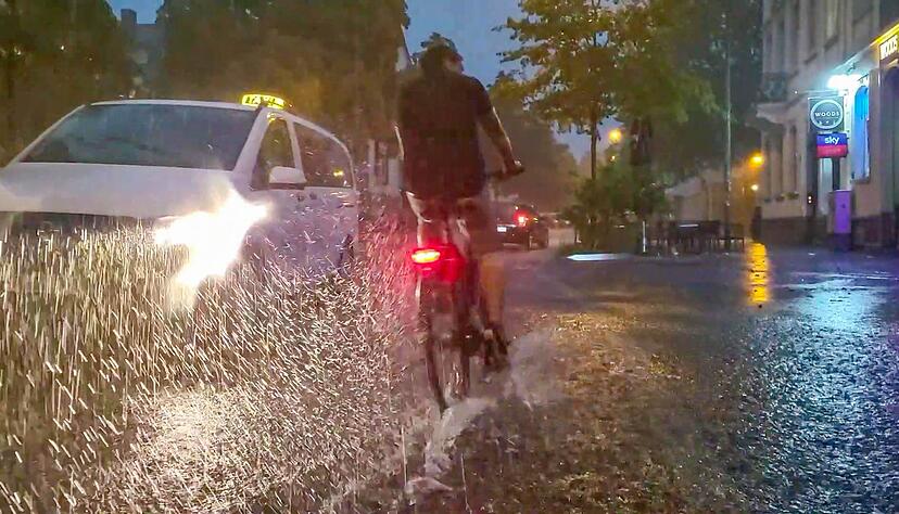 Ein Fahrradfahrer und ein Auto fahren über eine vom Regen überschwemmte Straße. Ein Fahrradfahrer und ein Auto fahren über eine vom Regen überschwemmte Straße.