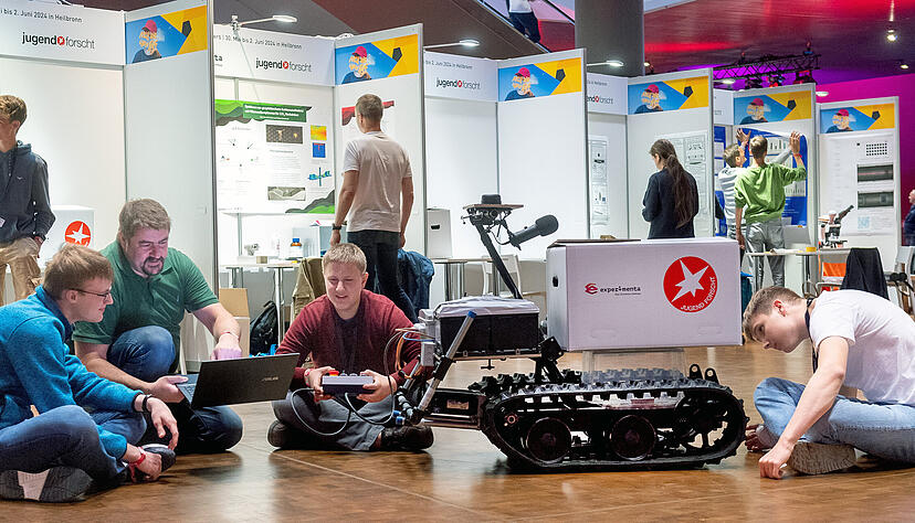 Der 17-J&auml;hrige Paul L&ouml;ffler (Mitte) aus Stuttgart pr&auml;sentiert die von ihm entwickelte, mit Lichtimpulsen gesteuerte "Robotic Tracking Platform". Die Maschine soll dem Menschen autonom und zuverl&auml;ssig folgen, etwa, um beim Einkauf schwere Waren zu tragen.