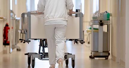 Eine Krankenpflegerin schiebt ein Krankenbett durch einen Krankenhausflur.