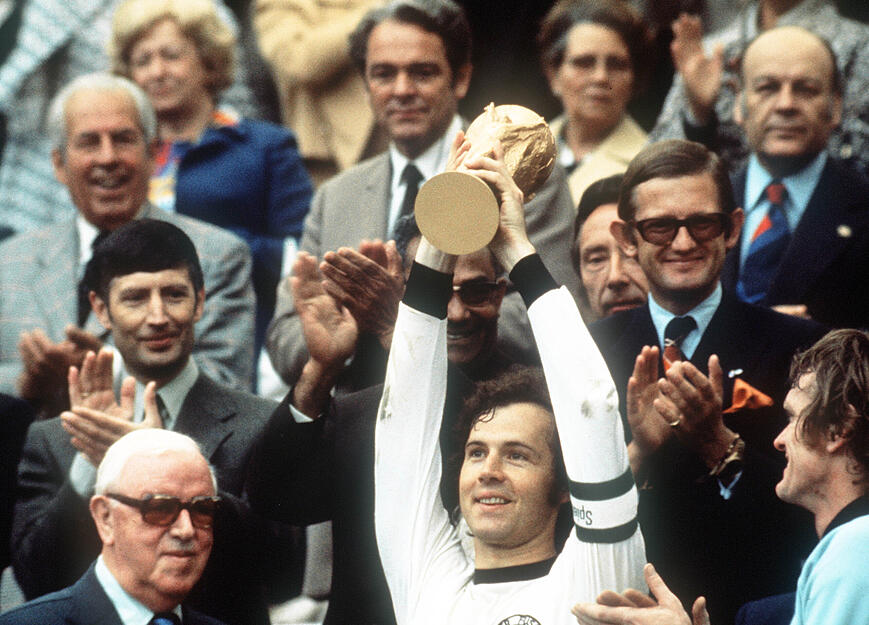 Kapitän Franz Beckenbauer (M) hebt an der Seite von Torhüter Sepp Maier (r) und dem englischen FIFA-Präsidenten Stanley Rous (l) im Olympiastadion nach dem Endspiel der Fußball-WM den eroberten WM-Pokal hoch.