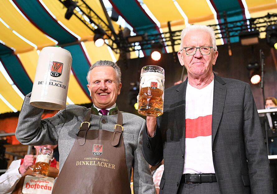 Frank Nopper (links, CDU), Oberbürgermeister von Stuttgart, und Winfried Kretschmann (Bündnis 90/Die Grünen), Ministerpräsident von Baden-Württemberg, stehen beim Stuttgarter Volksfest Cannstatter Wasen bei der Eröffnung mit Bierkrügen auf der Bühne.