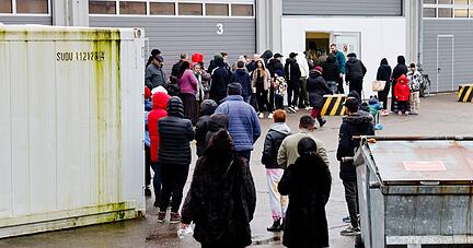 Menschen stehen bei einer Essenausgabe in der Landesunterkunft der Gemeinde Seeth im Kreis Nordfriesland Schlange.
