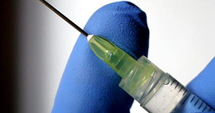 Eine Flüssigkeit tropft aus der Kanüle einer Spritze.