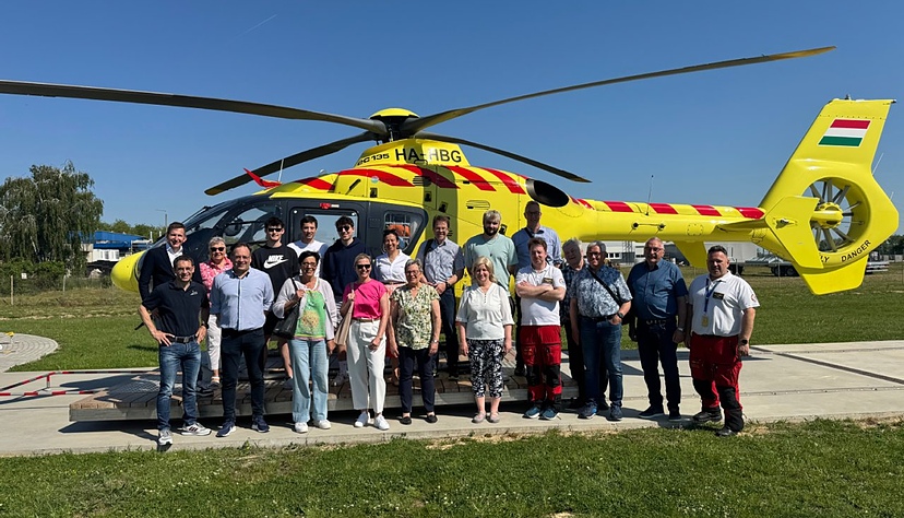 Vertreter der Kreisstadt Künzelsau besuchen die ungarische Partnerstadt Marcali und festigen die langjährige Verbindung beider Städte. Die Gruppe steht hier vor einem Hubschrauber der Luftrettungsbasis Marcali.