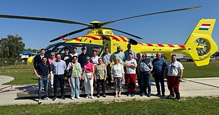 Vertreter der Kreisstadt Künzelsau besuchen die ungarische Partnerstadt Marcali und festigen die langjährige Verbindung beider Städte. Die Gruppe steht hier vor einem Hubschrauber der Luftrettungsbasis Marcali.