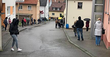 Mit ausreichend Abstand und Mund-Nasen-Schutz stehen Menschen in den Straßen von Neckarsulm-Obereisesheim und warten darauf, getestet zu werden. Um das Mobilnetz nicht zu überlasten, schalten sie ihr Mobiltelefon ab.