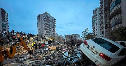 Notfallteams suchen nach Menschen in einem zerstörten Gebäude, während ein Auto auf den Trümmern liegt. Nach mehreren schweren Erdbeben in der türkisch-syrischen Grenzregion ist die Zahl der Toten auf mehr als 1900 gestiegen.