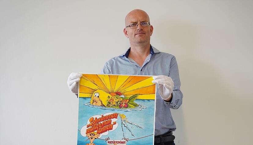 Historiker Sebastian Dörfler mit einem DLRG-Plakat aus den 1970er-Jahren, das in der Ausstellung zu sehen sein wird. Historiker Sebastian Dörfler mit einem DLRG-Plakat aus den 1970er-Jahren, das in der Ausstellung zu sehen sein wird.