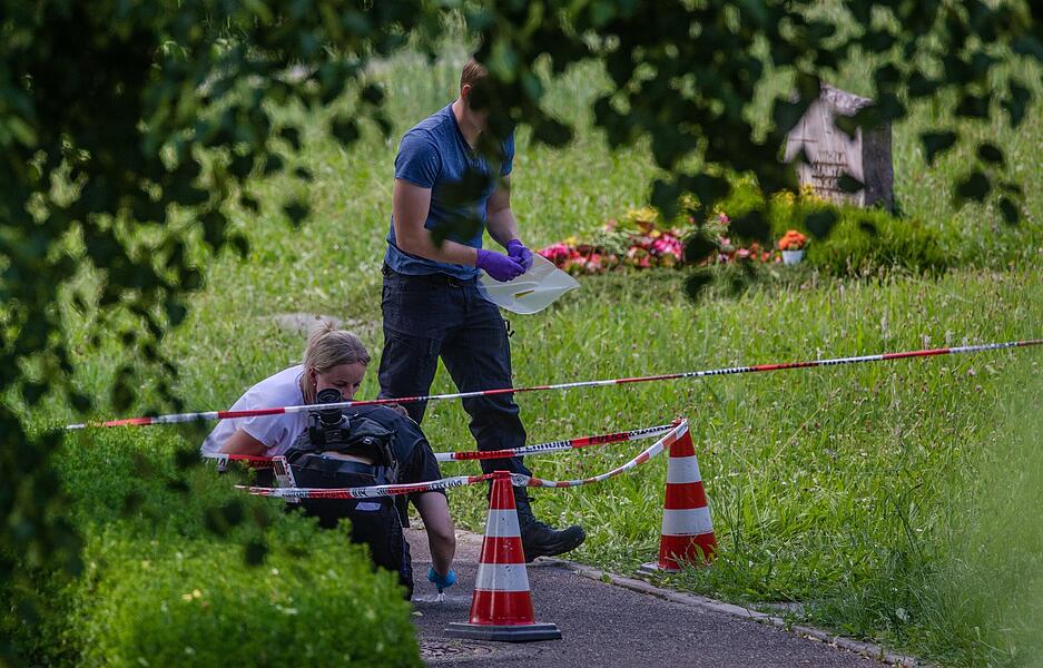 Mitarbeiter der Spurensicherung suchen nach Spuren an einem Tatort auf einem Friedhof. Durch den Wurf eines explodierenden Gegenstands auf eine Trauergemeinde gab es mehrere Verletzte. Mitarbeiter der Spurensicherung suchen nach Spuren an einem Tatort auf einem Friedhof. Durch den Wurf eines explodierenden Gegenstands auf eine Trauergemeinde gab es mehrere Verletzte.