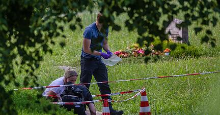Mitarbeiter der Spurensicherung suchen nach Spuren an einem Tatort auf einem Friedhof. Durch den Wurf eines explodierenden Gegenstands auf eine Trauergemeinde gab es mehrere Verletzte.