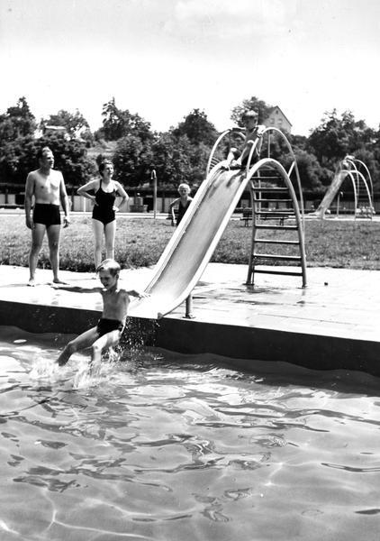 1953 - Mit viel Freude geht es über die Rutsche ab ins Wasser. Sind die Kinder beschäftigt,  können die Eltern das schöne Wetter genießen.