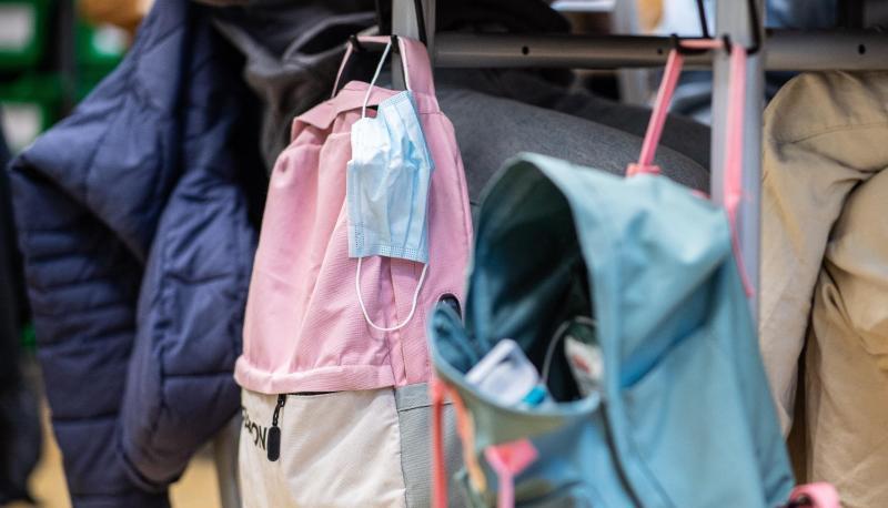 Masken hängen in einem Klassenzimmer an Rucksäcken von Schülern. Masken hängen in einem Klassenzimmer an Rucksäcken von Schülern.