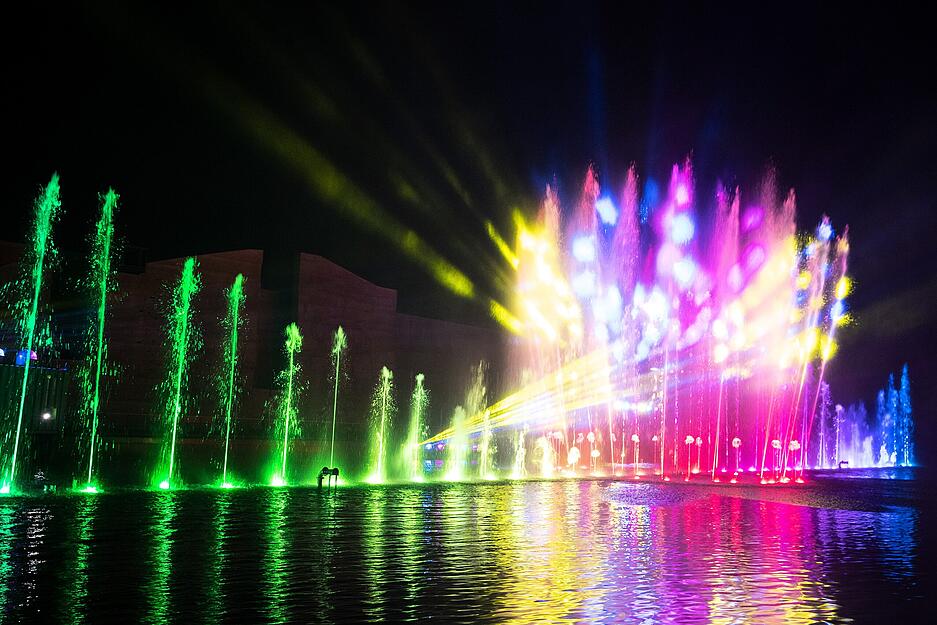 Sobald die Dämmerung einsetzt, füllen sich die Ufer des Karlssees mit Menschen. Die spektakulären Wassershows locken tausende Besucher an. Im Hintergrund ist ein Bereich der Kletterwand sichtbar.