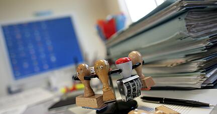 Ein Stempelkarussell steht neben einem Stapel Akten auf einem Schreibtisch in einer Behörde. Ein Stempelkarussell steht neben einem Stapel Akten auf einem Schreibtisch in einer Behörde.