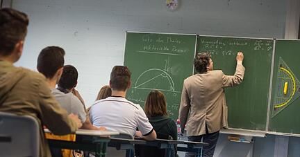 Ein Lehrer schreibt w&auml;hrend des Matheunterrichts einer Abiturklasse an die Tafel.