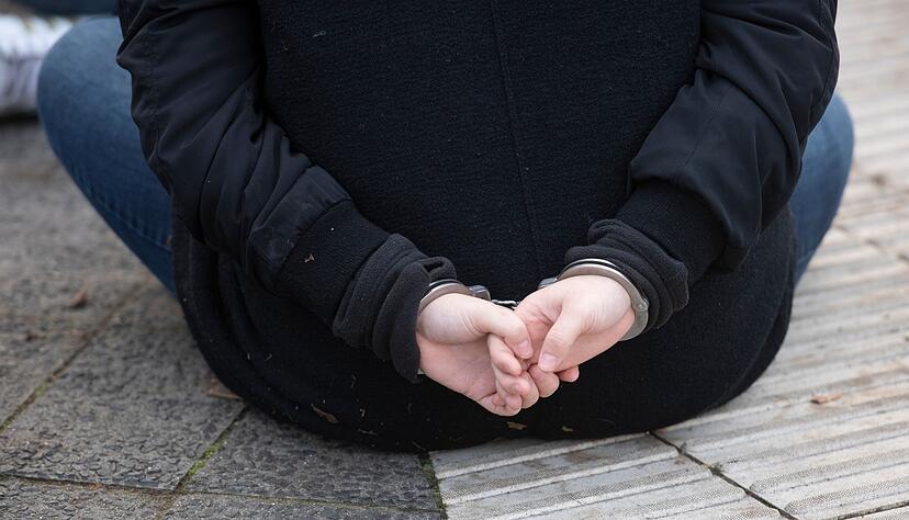 Eine Aktivistin der Gruppe "Letzte Generation" sitzt mit Handschellen gefesselt auf einer Straße. Eine Aktivistin der Gruppe "Letzte Generation" sitzt mit Handschellen gefesselt auf einer Straße.