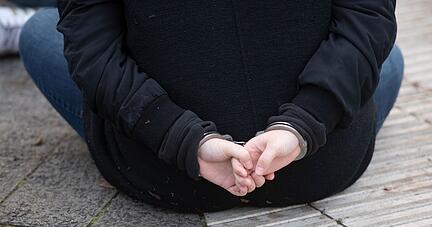 Eine Aktivistin der Gruppe "Letzte Generation" sitzt mit Handschellen gefesselt auf einer Straße.